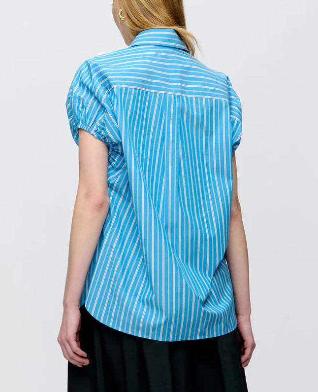 A person is seen from the back wearing the Lecce Stripe Top by Callas Milano, a relaxed-fit blue and white striped short-sleeved shirt, styled with a black skirt against a light background.
