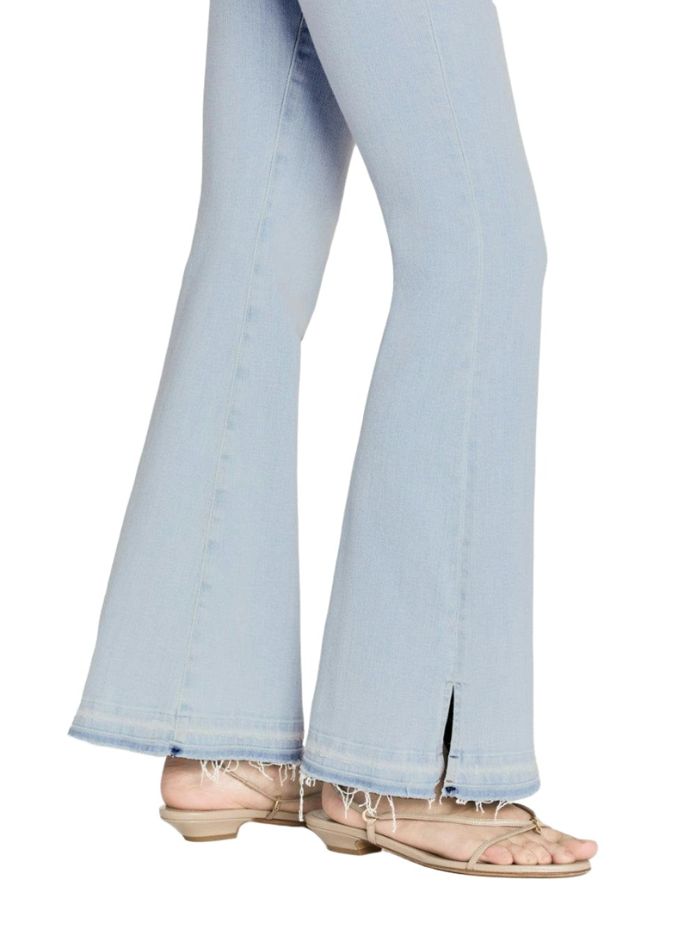 Person wearing Frame Le Easy Flare Released Fray Side Slit jeans with frayed hems and pink sandals, isolated on white background.