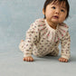 A baby wearing the Louise Misha Baby Girls’ Rosaline Sweatshirt crawls on a light blue surface, gazing slightly upward with a neutral expression.