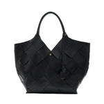 The Lili Braided Leather Tote by Anine Bing is a spacious black bag crafted from leather with a braided finish, featuring two top handles and adorned with a small gold emblem on the front, photographed against a white background.