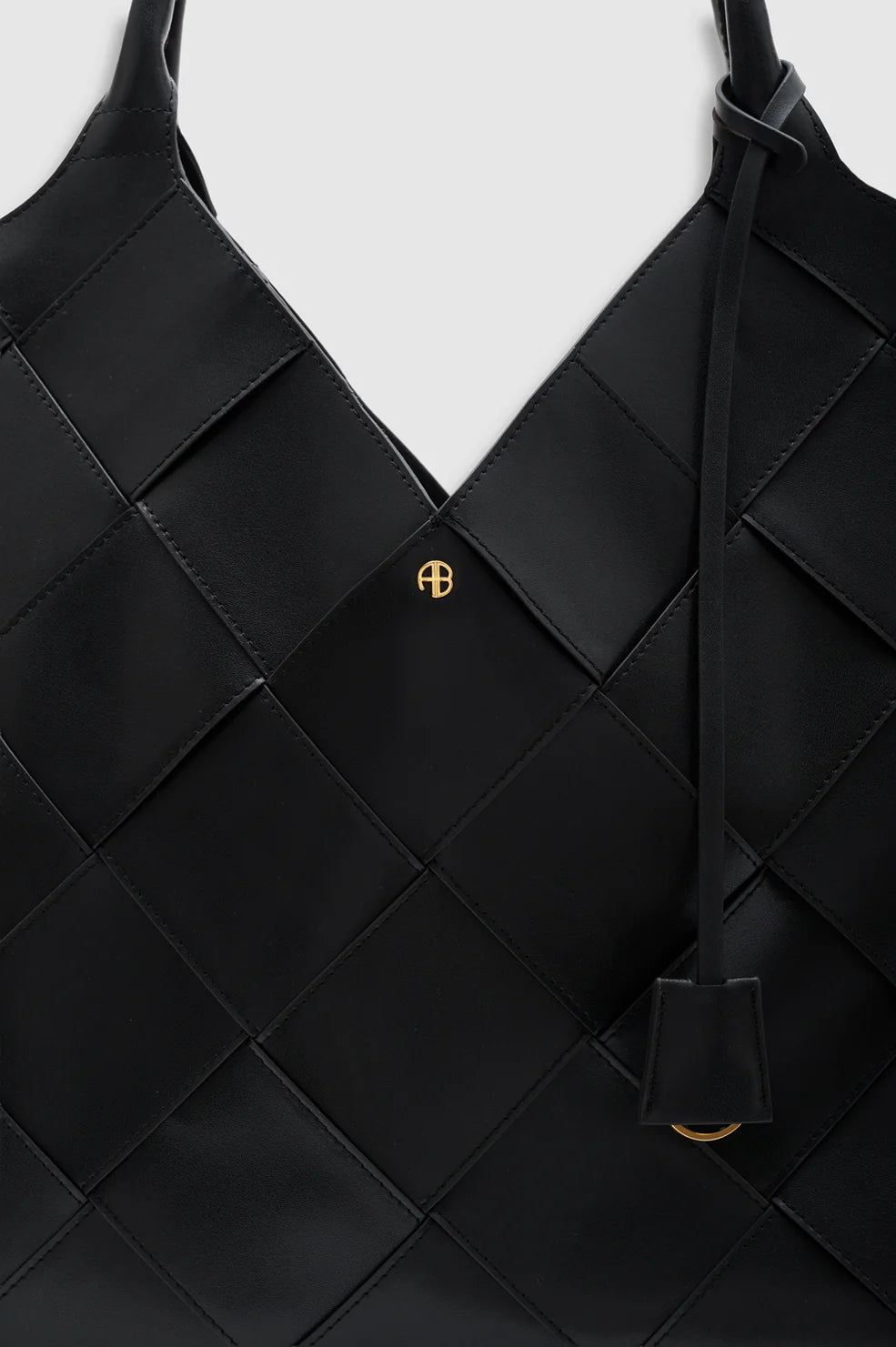 Close-up of the Anine Bing Lili Braided Leather Tote, featuring a black braided leather finish, gold AB logo, and a leather strap with a small tag.