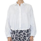 A person wearing the Callas Milano Lille Top, a loose-fitting cotton poplin shirt with a point collar, paired with black-and-white floral patterned pants, stands against a plain background.