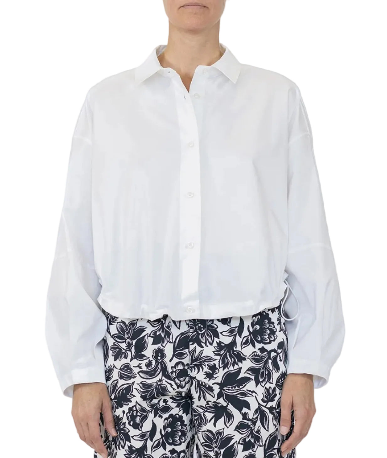 A person wearing the Callas Milano Lille Top, a loose-fitting cotton poplin shirt with a point collar, paired with black-and-white floral patterned pants, stands against a plain background.