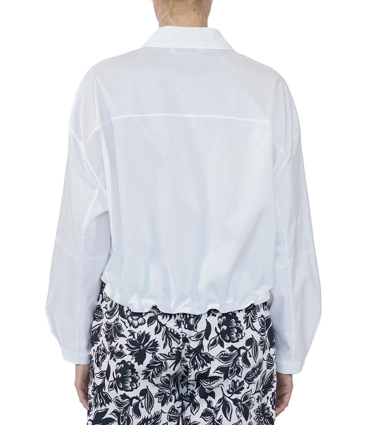 A person is seen from the back wearing the Callas Milano Lille Top, a loose white cotton poplin point collar shirt, paired with black-and-white floral patterned pants against a plain background.