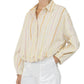 A person wearing the Callas Milano Lille Top—a loose, long-sleeve cotton poplin shirt with pastel stripes and a point collar—paired with white pants, photographed from the waist up.