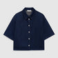 The Anine Bing Lincoln Shirt, a dark blue lightweight denim piece featuring short sleeves, a collar, and front pearl buttons, is displayed laid flat on a plain light background.