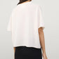 A woman with long dark hair is shown from the back, wearing the Lisa Yang Cila Cashmere T-Shirt in white and a black skirt against a plain background.