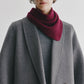 A person wearing a grey coat and sweater, styled with the Lisa Yang Florianne Scarf in burgundy draped around their neck, stands against a plain light background.