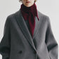 A person wearing a grey wool coat and the Lisa Yang Florianne Scarf in burgundy, tied at the neck, stands against a plain white background.