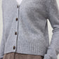 A person is wearing the Marionette Cardigan by Lisa Yang, a lightweight, light gray buttoned cardigan, over a white top and paired with high-waisted brown pants.