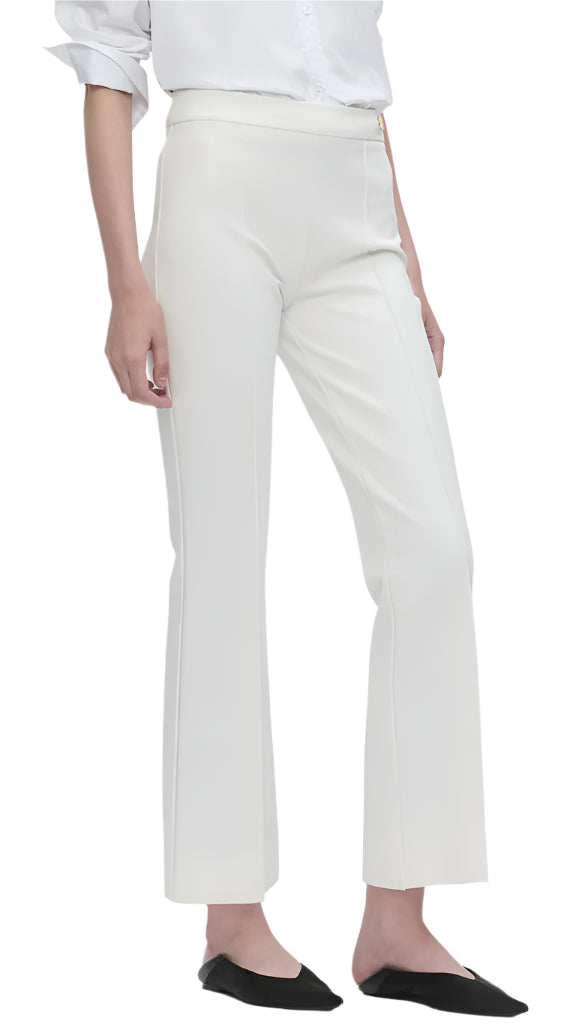 A person wearing Callas Milano's Lola Pant, a high-rise white dress pant, paired with a white shirt and black flat shoes, is shown standing straight from upper body to feet.