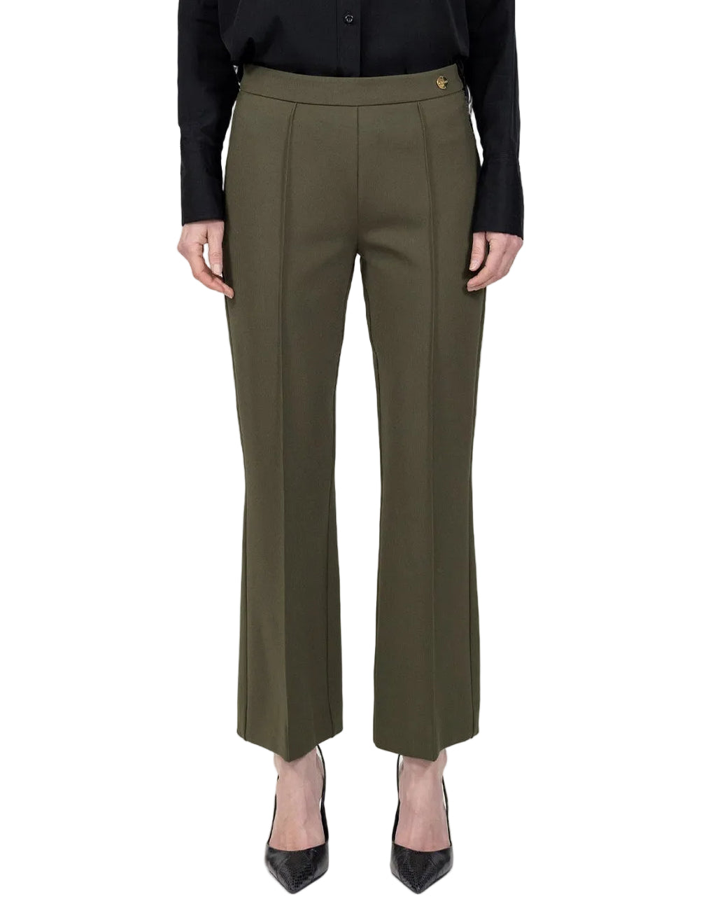 A person is wearing the Lola Pant by Callas Milano—olive green tailored flared trouser pants crafted from stretch crepe knit—paired with a black long-sleeve shirt and black pointed-toe heels, standing against a white background.