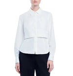 A person wearing the Lela Rose Cotton Poplin Layered Shirt—a white long-sleeve top with a cropped overlay—paired with black pants, standing against a white background.
