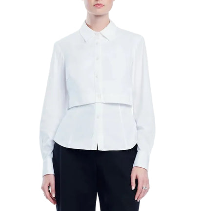 A person wearing the Lela Rose Cotton Poplin Layered Shirt—a white long-sleeve top with a cropped overlay—paired with black pants, standing against a white background.