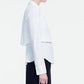 A person stands in profile against a plain white background, wearing the Lela Rose Cotton Poplin Layered Shirt in white with black pants.
