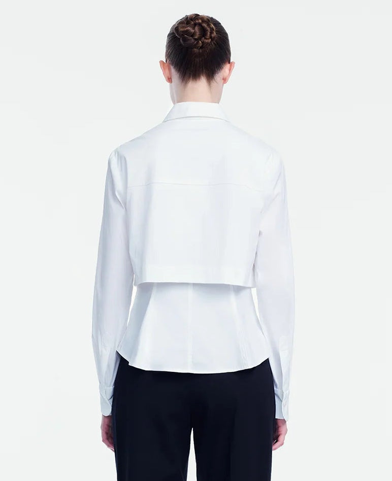 A person stands with their back to the camera against a plain background, wearing the Lela Rose Cotton Poplin Layered Shirt paired with black pants and a white relaxed fit cropped jacket.