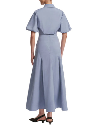 A person wearing Lela Rose's Seam Detail Skirt in light blue with a collared, short-sleeve top—an absolute wardrobe essential—and black low-heeled slingback shoes, shown from the back.