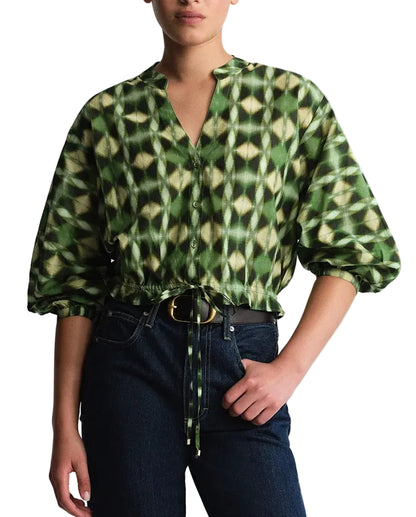 A person wearing the Cara Cara Perrin Top—a green patterned cotton voile blouse with a drawstring waist—paired with dark blue jeans, standing with one hand in their pocket against a white background.