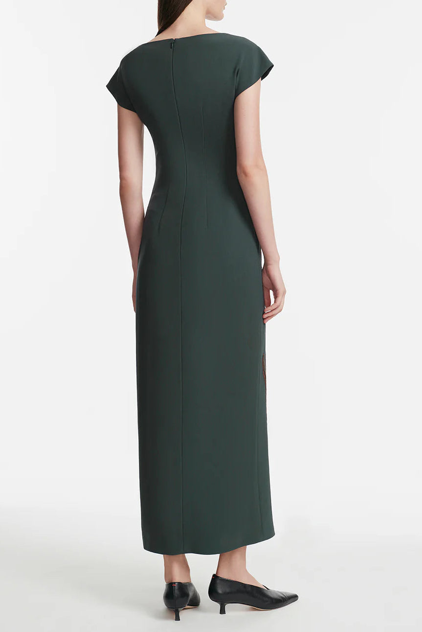 A person stands facing away in a dark green, short-sleeve, ankle-length Lela Rose Floral Fluid Crepe Cascade Dress with a back zipper and black low-heeled shoes against a plain white background.