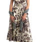 A woman wearing the Cara Cara Sawyer Dress—a cream-colored, short-sleeve, floral print belted A-line dress—paired with black knee-high boots and a gray sweater draped over her arms.