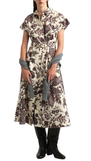 A woman wearing the Cara Cara Sawyer Dress—a cream-colored, short-sleeve, floral print belted A-line dress—paired with black knee-high boots and a gray sweater draped over her arms.