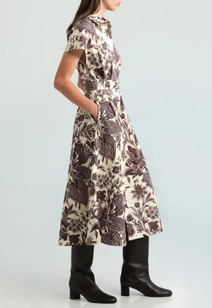 A woman wearing the Sawyer Dress by Cara Cara—a short-sleeved, floral-patterned poplin midi dress with pockets—paired with knee-high black boots, stands against a plain light background.