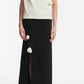 A person wearing the Lela Rose Drop Flower Cowl Neck Top stands against a plain background, paired with a black ankle-length skirt featuring a front slit and black pointed-toe shoes.