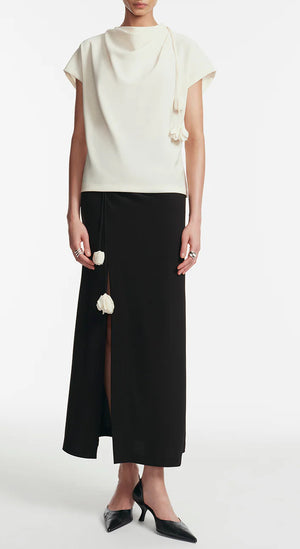 A person wearing the Lela Rose Drop Flower Cowl Neck Top stands against a plain background, paired with a black ankle-length skirt featuring a front slit and black pointed-toe shoes.