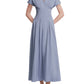 A woman wears the Lela Rose Smocked Back Dress in light blue cotton poplin, featuring a pleat-tailored bodice, V-neckline, ankle-length pleated skirt, and brown shoes.