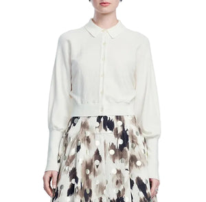 A woman wearing the Lela Rose Cropped Dolman Cardigan—a white button-up with a collar and relaxed fit—paired with a high-waisted skirt featuring a black, brown, and white abstract dot pattern.