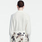 A woman with brown hair in a bun is shown from the back against a plain light background, wearing the Lela Rose Cropped Dolman Cardigan and a patterned skirt.