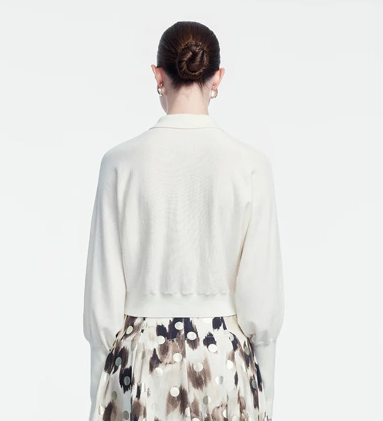 A woman with brown hair in a bun is shown from the back against a plain light background, wearing the Lela Rose Cropped Dolman Cardigan and a patterned skirt.