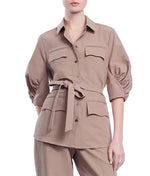 A woman wearing the Lela Rose Melange Crepe Camp Shirt, a tan melange top with a classic silhouette, four pockets, and three-quarter ruched sleeves, paired with matching textured tan pants.