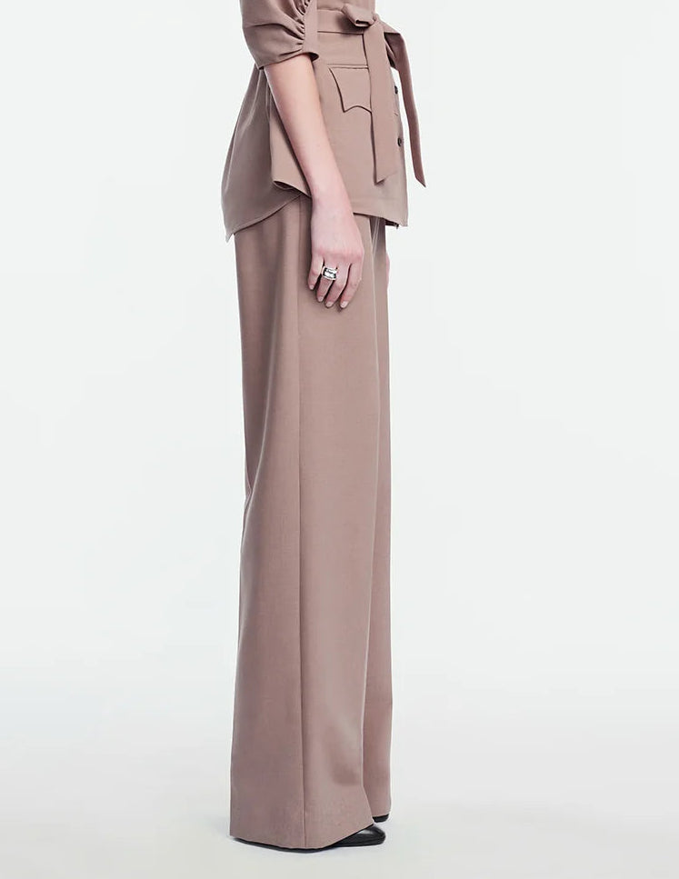 A person stands in side profile against a plain white background, wearing the Lela Rose Melange Crepe High Waisted Pant paired with a taupe belted blouse featuring pocket flaps and a tailored leg.