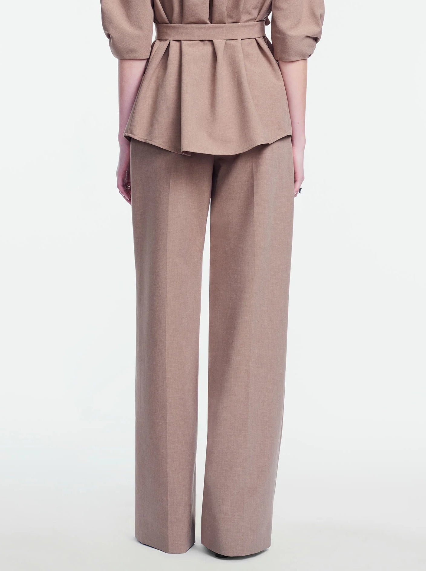 A person stands facing away against a plain white background, wearing the Lela Rose Melange Crepe High Waisted Pant with a tailored leg, paired with a matching beige melange crepe tailored jacket featuring a peplum waist.