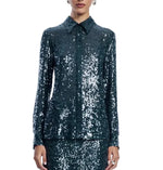 A person wearing the Lela Rose Sequin Lucy Shirt—a dark green, long-sleeved sequin top—paired with a matching skirt, stands against a white background, showcasing a true statement piece that exudes sophistication.