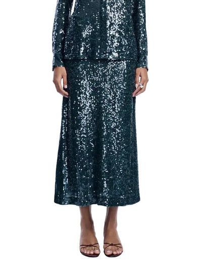 A person wearing the Lela Rose Sequin Skirt, featuring a long-sleeve, dark green sequined top and a matching midi skirt, styled with open-toe sandals.