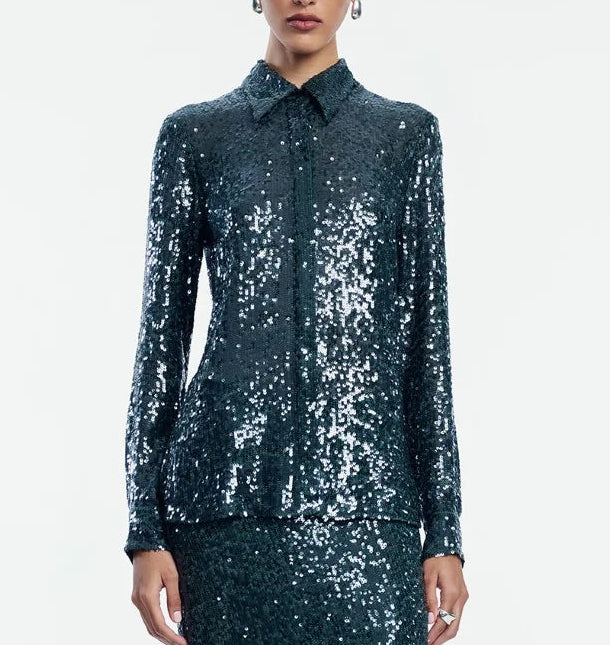 A person wearing the Lela Rose Sequin Lucy Shirt—a long-sleeve, dark green sequin top—paired with a matching skirt, stands against a plain white background. The Sequin Lucy Shirt from Lela Rose is a bold statement piece that effortlessly elevates the entire look.