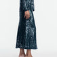 A person is dressed in the Lela Rose Sequin Skirt paired with a matching top, featuring shimmering sequins and styled with strappy heeled sandals, standing against a plain white background.