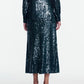Wearing the Lela Rose Sequin Skirt, a person is shown from the back in a matching dark green, long-sleeve sequin top and midi skirt ensemble embellished with shimmering sequins, paired with open-heeled sandals.