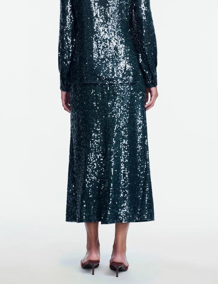 Wearing the Lela Rose Sequin Skirt, a person is shown from the back in a matching dark green, long-sleeve sequin top and midi skirt ensemble embellished with shimmering sequins, paired with open-heeled sandals.