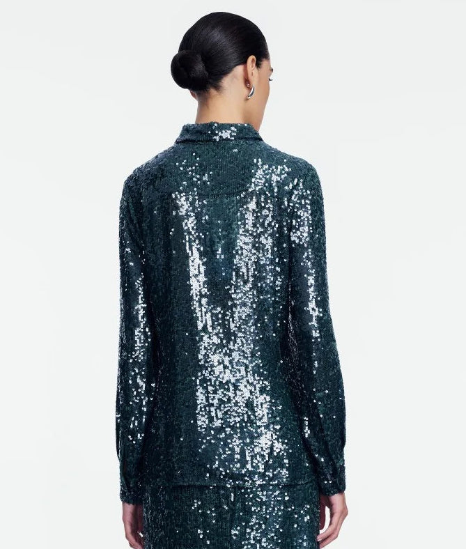 A person with dark hair in a low bun is shown from behind, wearing a statement piece: the Lela Rose Sequin Lucy Shirt—a long-sleeved, dark green sequin top—paired with a matching skirt against a plain white background.
