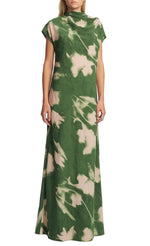 A woman wears the Lela Rose Abstract Floral Crepe Draped Gown, a floor-length green dress with white abstract leaf patterns and short sleeves, featuring a straight-fit silhouette against a plain background.