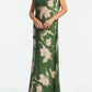 A person wears the Lela Rose Abstract Floral Crepe Draped Gown, a floor-length, short-sleeve dress with a straight-fit silhouette, featuring green and beige abstract florals, standing against a plain white background.