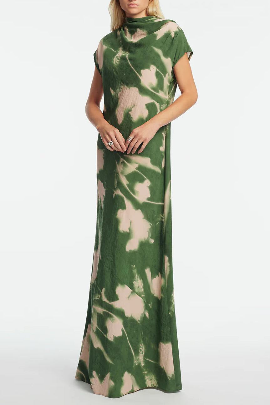 A person wears the Lela Rose Abstract Floral Crepe Draped Gown, a floor-length, short-sleeve dress with a straight-fit silhouette, featuring green and beige abstract florals, standing against a plain white background.
