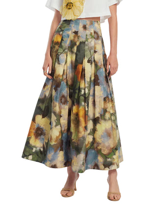 A woman wears the Lela Rose Floral Printed Cotton Skirt, a high-waisted, ankle-length A-line with pleated brushstroke florals, styled with a white cropped top and beige open-toe heels.
