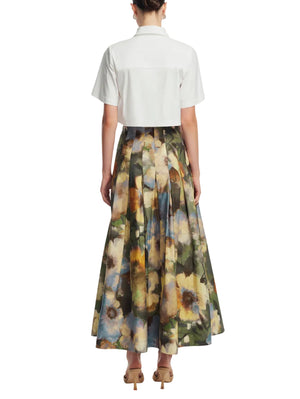 A person stands facing away, wearing the Lela Rose Peony Embroidered Cropped Shirt with a high-waisted, pleated, ankle-length floral skirt and beige heels.