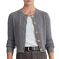 Outfitted in the Cara Cara Ellery Cardigan—a grey knit featuring gold floral buttons—layered over a white shirt, paired with plaid trousers and finished with a black belt with a gold buckle, this classic ensemble is the perfect wardrobe staple.
