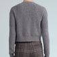 A person is facing away, wearing the Cara Cara Ellery Cardigan—a gray long-sleeve sweater with gold floral buttons—paired with brown plaid pants, set against a plain light background.