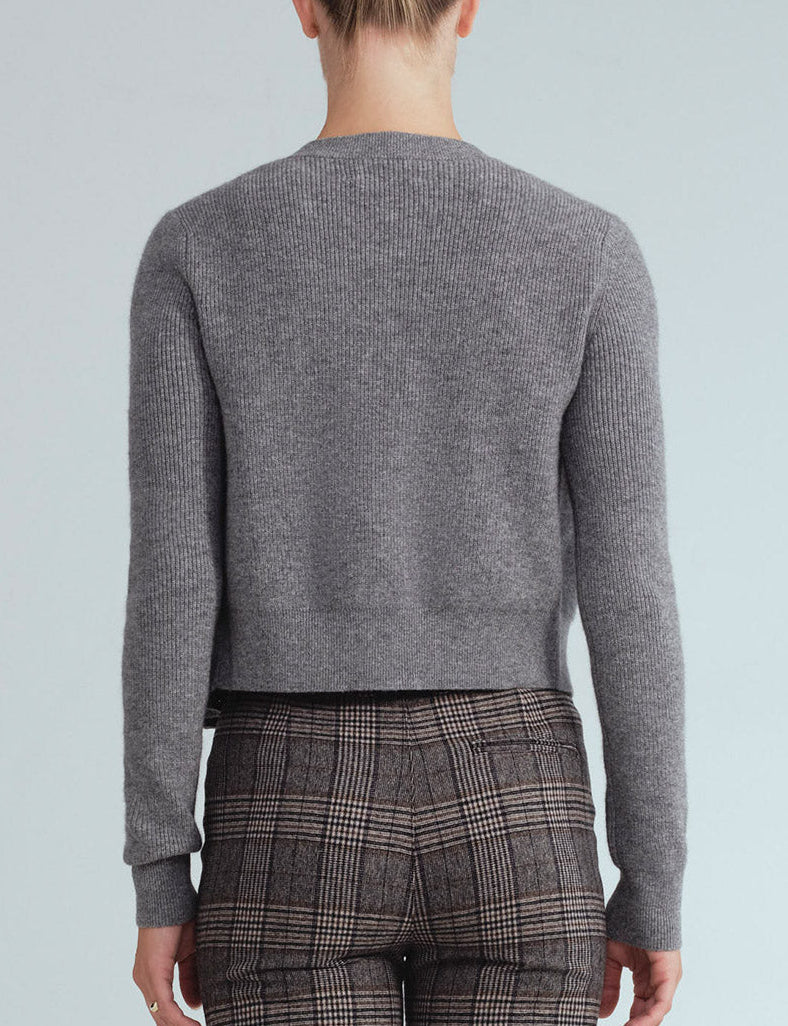 A person is facing away, wearing the Cara Cara Ellery Cardigan—a gray long-sleeve sweater with gold floral buttons—paired with brown plaid pants, set against a plain light background.